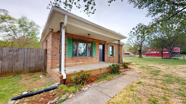 view of front of property featuring brick siding, a porch, fence, and a front yard