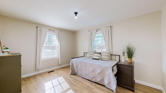bedroom with baseboards, visible vents, multiple windows, and light wood finished floors