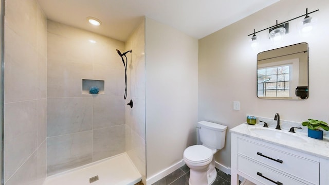 bathroom featuring tile patterned floors, a tile shower, toilet, baseboards, and vanity