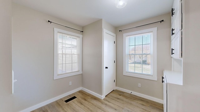 doorway with light wood-type flooring, visible vents, and baseboards