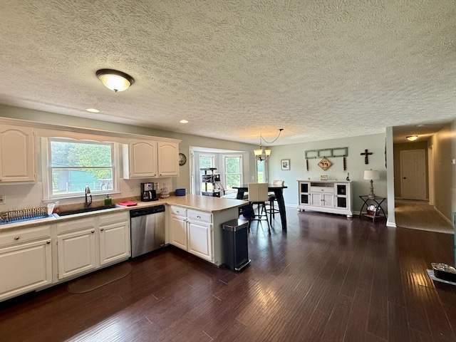 kitchen with stainless steel dishwasher, a sink, a textured ceiling, a peninsula, and dark wood-style flooring