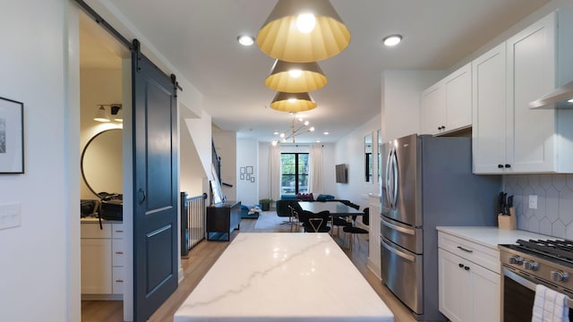 kitchen featuring white cabinets, decorative backsplash, appliances with stainless steel finishes, and a barn door