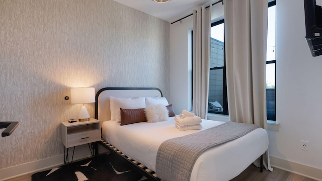 bedroom featuring wallpapered walls, wood finished floors, and baseboards
