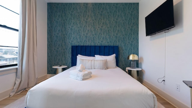 bedroom featuring an accent wall, wood finished floors, baseboards, and wallpapered walls