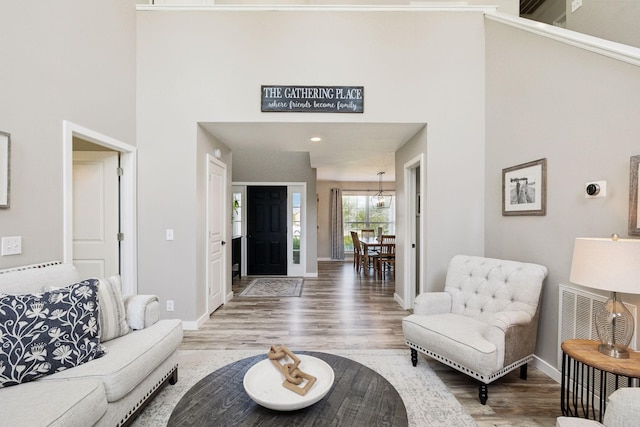 living area with baseboards, a towering ceiling, wood finished floors, and visible vents