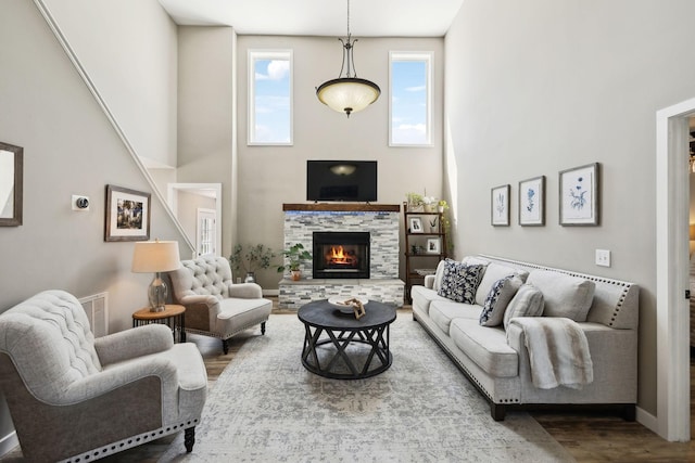 living room with visible vents, wood finished floors, a stone fireplace, baseboards, and a high ceiling