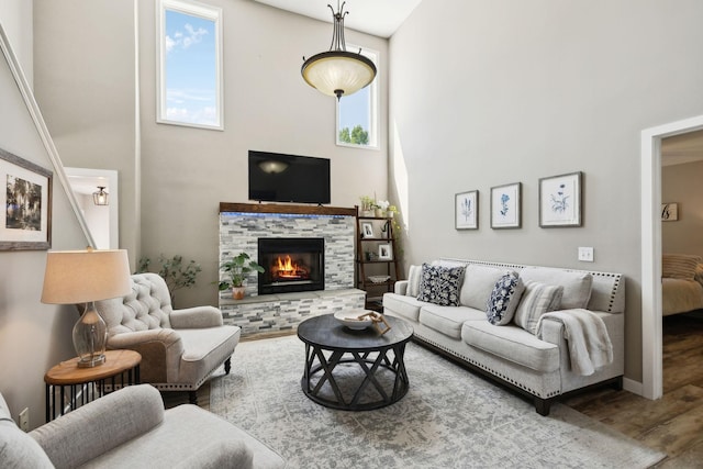 living room with a stone fireplace, wood finished floors, and a towering ceiling