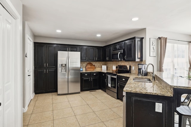 kitchen featuring stainless steel appliances, dark cabinets, a sink, and a peninsula