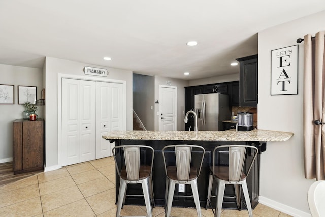 kitchen featuring a kitchen bar, stainless steel fridge with ice dispenser, baseboards, a peninsula, and dark cabinets