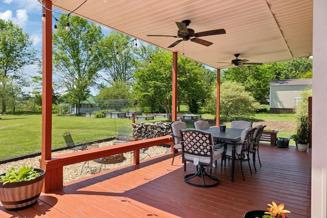 wooden deck featuring an outdoor structure, ceiling fan, a lawn, a storage shed, and outdoor dining space