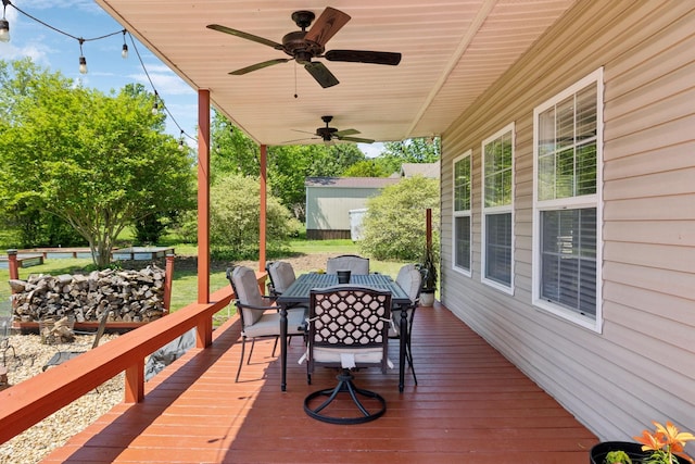 wooden terrace with a storage shed, outdoor dining space, ceiling fan, and an outbuilding