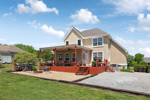 back of property featuring ceiling fan, a deck, an outdoor fire pit, a yard, and stucco siding
