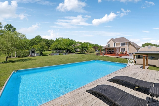outdoor pool featuring a lawn, a storage shed, a wooden deck, and an outbuilding