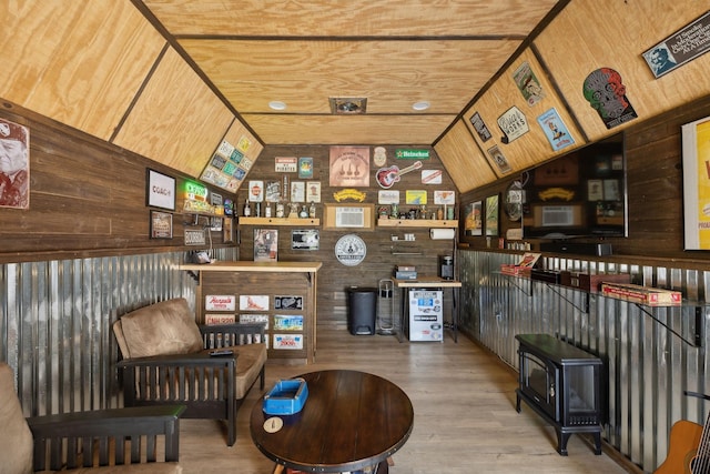 bar featuring a wood stove, wood finished floors, wooden walls, and vaulted ceiling