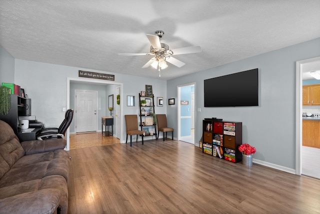 living area with wood finished floors, a textured ceiling, baseboards, and ceiling fan