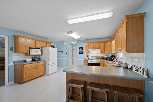 kitchen featuring tasteful backsplash, white appliances, light wood finished floors, a peninsula, and under cabinet range hood