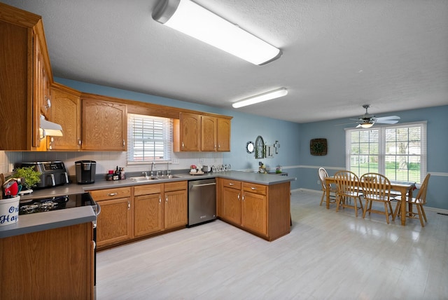kitchen with light wood finished floors, a peninsula, stainless steel dishwasher, a sink, and under cabinet range hood