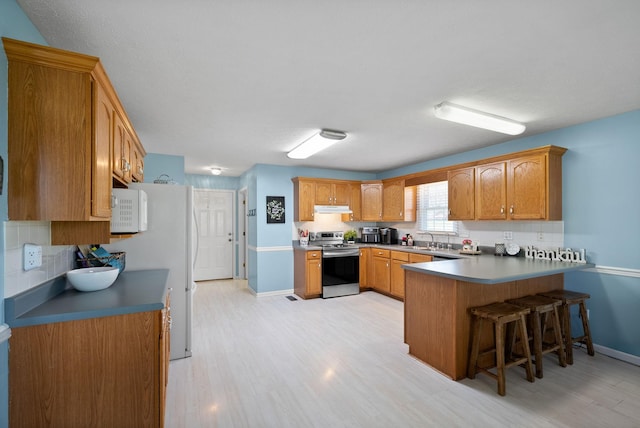 kitchen with a peninsula, light wood-style flooring, baseboards, white appliances, and under cabinet range hood