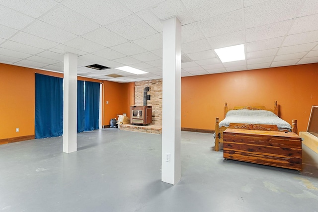 finished below grade area with baseboards, visible vents, a wood stove, and a paneled ceiling
