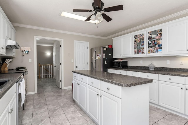 kitchen featuring under cabinet range hood, dark countertops, ornamental molding, a center island, and stainless steel fridge