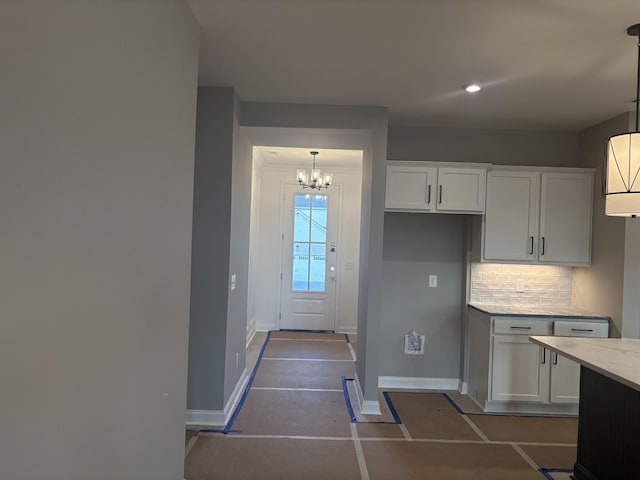 kitchen featuring a chandelier, baseboards, white cabinetry, tasteful backsplash, and decorative light fixtures