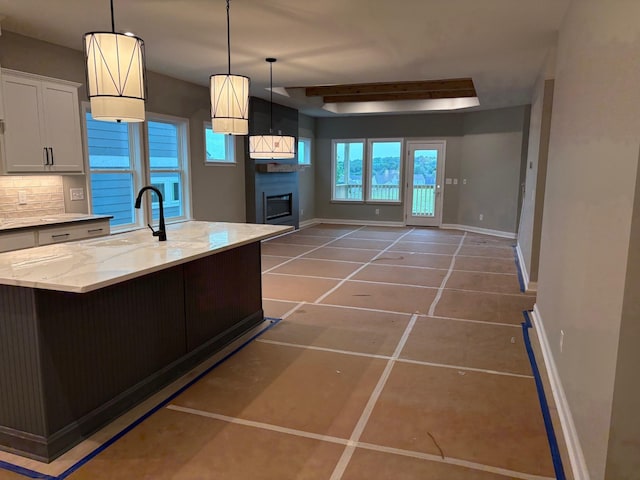 kitchen featuring a glass covered fireplace, a sink, light stone counters, baseboards, and tile patterned flooring