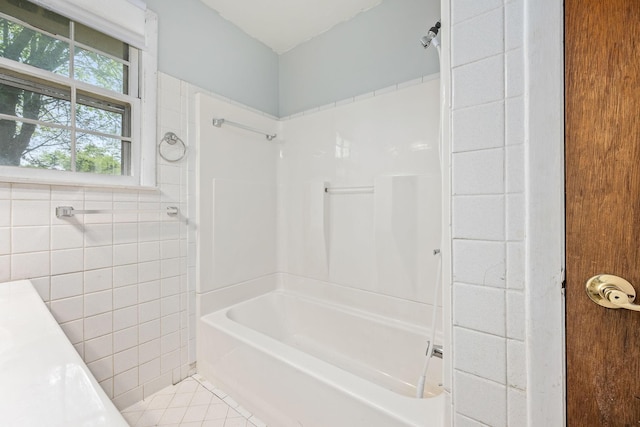 bathroom with tile walls, bathing tub / shower combination, and tile patterned flooring