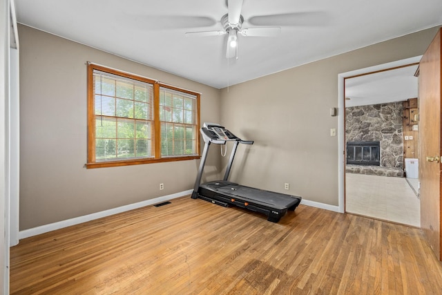 workout room featuring wood finished floors, ceiling fan, a fireplace, baseboards, and visible vents