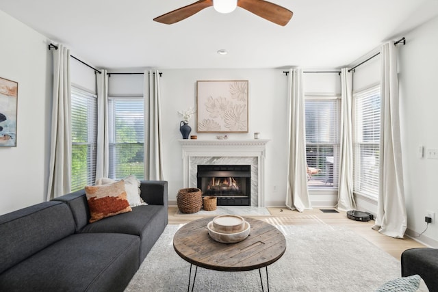 living area with a high end fireplace, baseboards, a ceiling fan, and wood finished floors