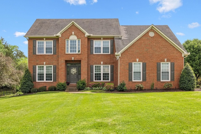 colonial inspired home featuring brick siding, a front yard, and roof with shingles