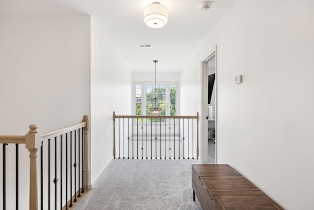corridor with visible vents, carpet, an upstairs landing, and an inviting chandelier