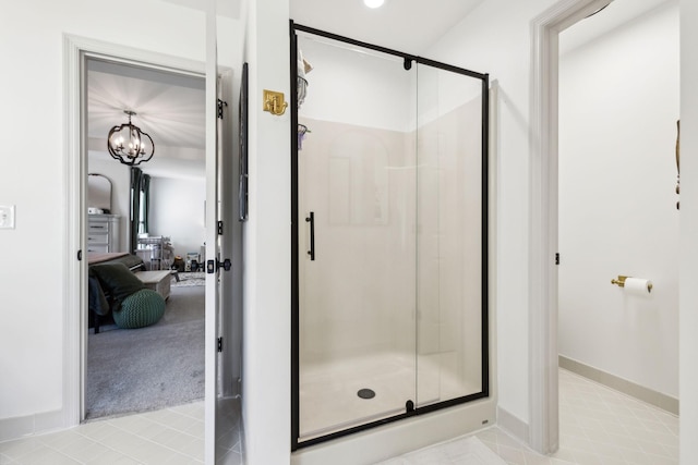 ensuite bathroom featuring baseboards, tile patterned floors, a stall shower, and a notable chandelier