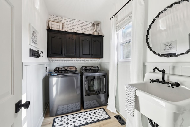 washroom with cabinet space, separate washer and dryer, a sink, and a wainscoted wall