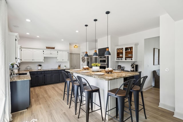 kitchen featuring a breakfast bar area, backsplash, white cabinetry, double oven, and light wood-style flooring