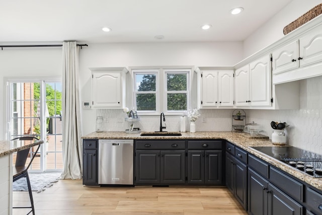 kitchen with stainless steel dishwasher, black electric stovetop, white cabinets, a sink, and backsplash