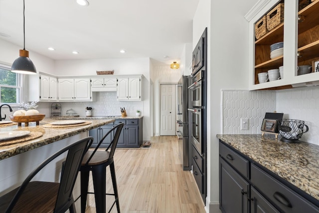 kitchen featuring white cabinets, tasteful backsplash, light stone counters, light wood-style flooring, and decorative light fixtures