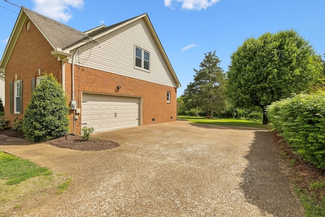 view of side of home featuring an attached garage, driveway, crawl space, and brick siding