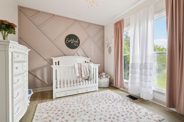 bedroom with baseboards, visible vents, a crib, and wood finished floors