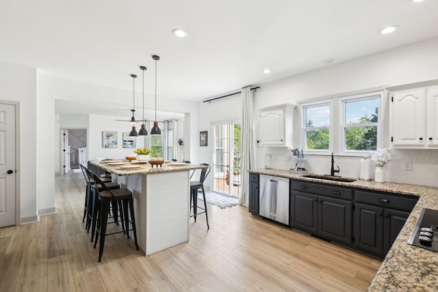 kitchen featuring a sink, a kitchen breakfast bar, white cabinetry, backsplash, and stainless steel dishwasher