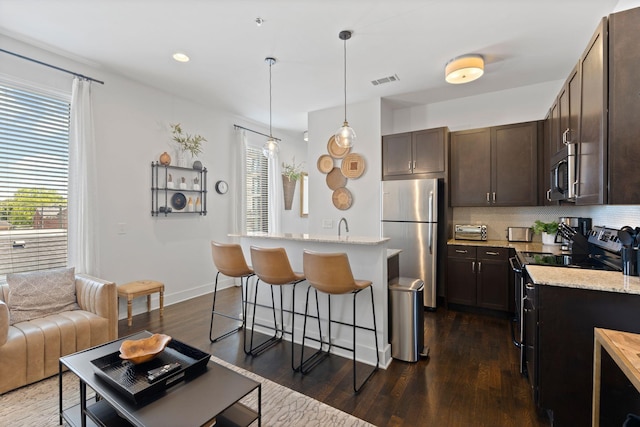 kitchen featuring visible vents, dark brown cabinetry, a kitchen bar, appliances with stainless steel finishes, and dark wood-style flooring