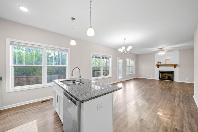 kitchen featuring light wood finished floors, a kitchen island with sink, stainless steel dishwasher, a sink, and baseboards