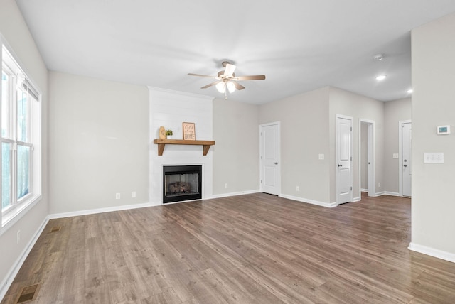 unfurnished living room featuring a ceiling fan, wood finished floors, visible vents, and a fireplace