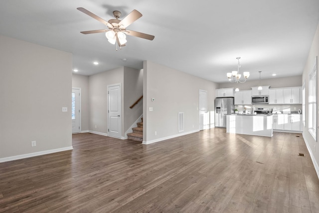 unfurnished living room featuring wood finished floors, stairs, ceiling fan with notable chandelier, baseboards, and visible vents