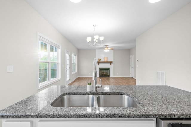 kitchen with dark stone counters, wood finished floors, a sink, a chandelier, and a fireplace