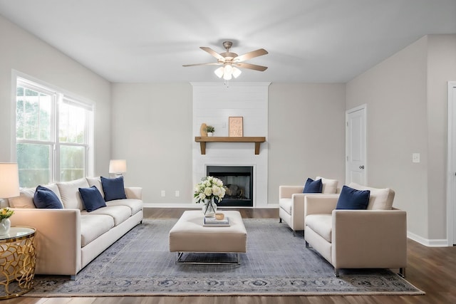 living room featuring ceiling fan, baseboards, a large fireplace, and wood finished floors