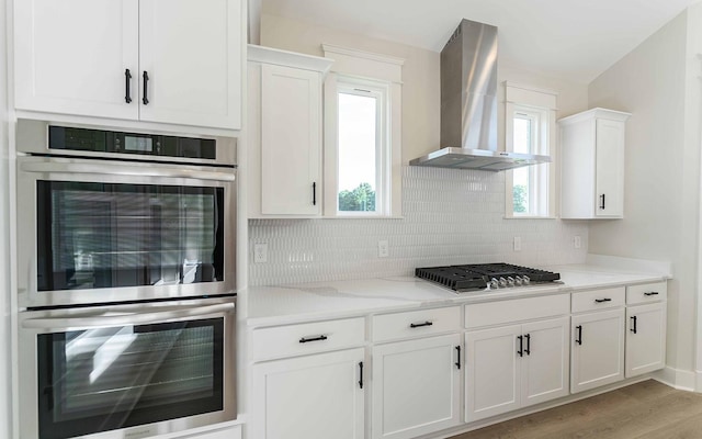 7295 NW Hwy, Fairview, TN 37062 - kitchen featuring stainless steel appliances, wall chimney range hood, white cabinetry, tasteful backsplash, and light wood-style floors