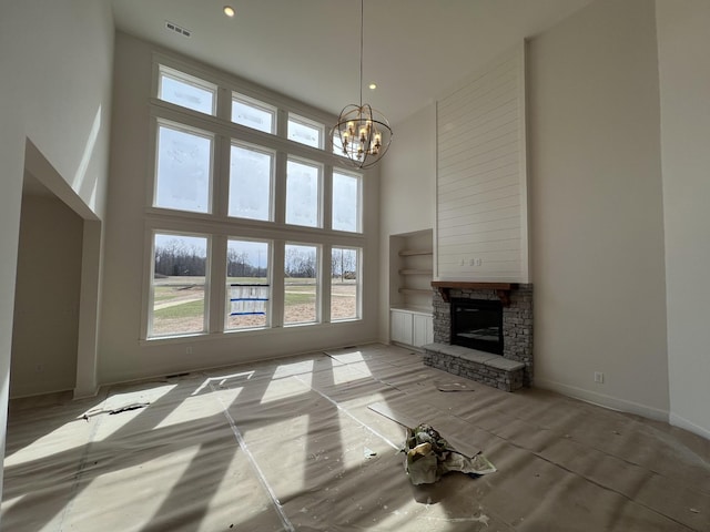 unfurnished living room with a stone fireplace, a healthy amount of sunlight, a towering ceiling, and an inviting chandelier