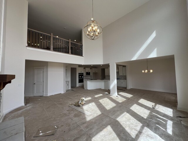 unfurnished living room featuring a chandelier, a high ceiling, and baseboards