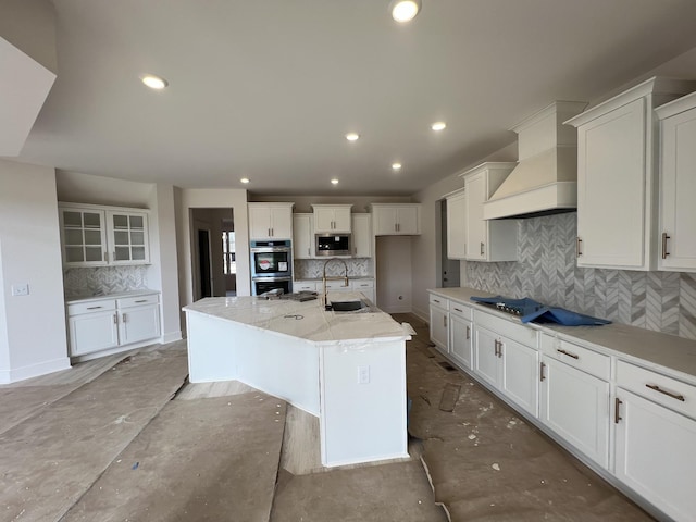 kitchen with a sink, tasteful backsplash, white cabinetry, custom range hood, and appliances with stainless steel finishes