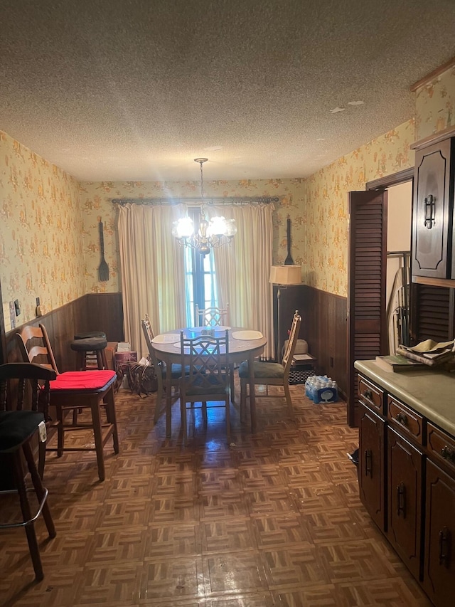 dining space featuring wallpapered walls, a textured ceiling, and a wainscoted wall